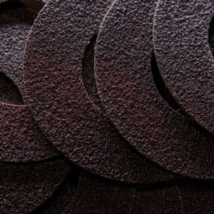 Close-up of overlapping circular pieces of coarse, dark brown sandpaper, showing their rough, gritty texture in detail.